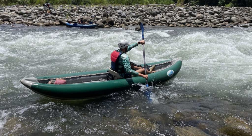 A person wearing safety gear paddles a watercraft through small rapids